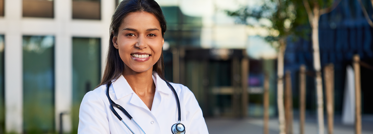 Vrolijke arts staat met haar armen over elkaar buiten voor een ziekenhuis