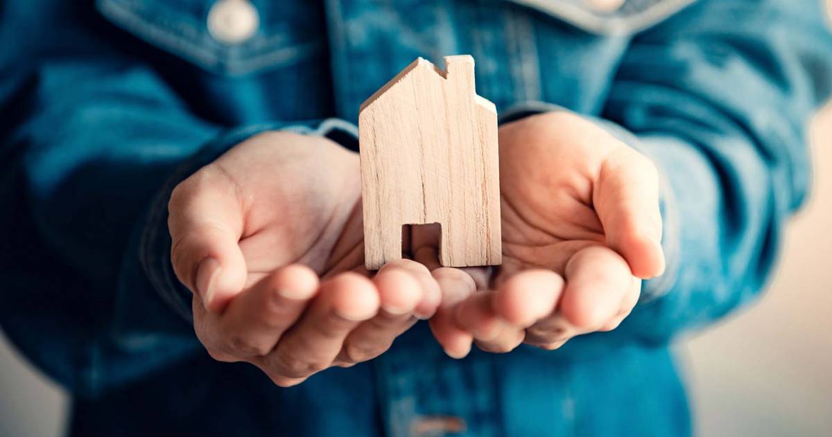 Twee handen die een houten huisje dragen