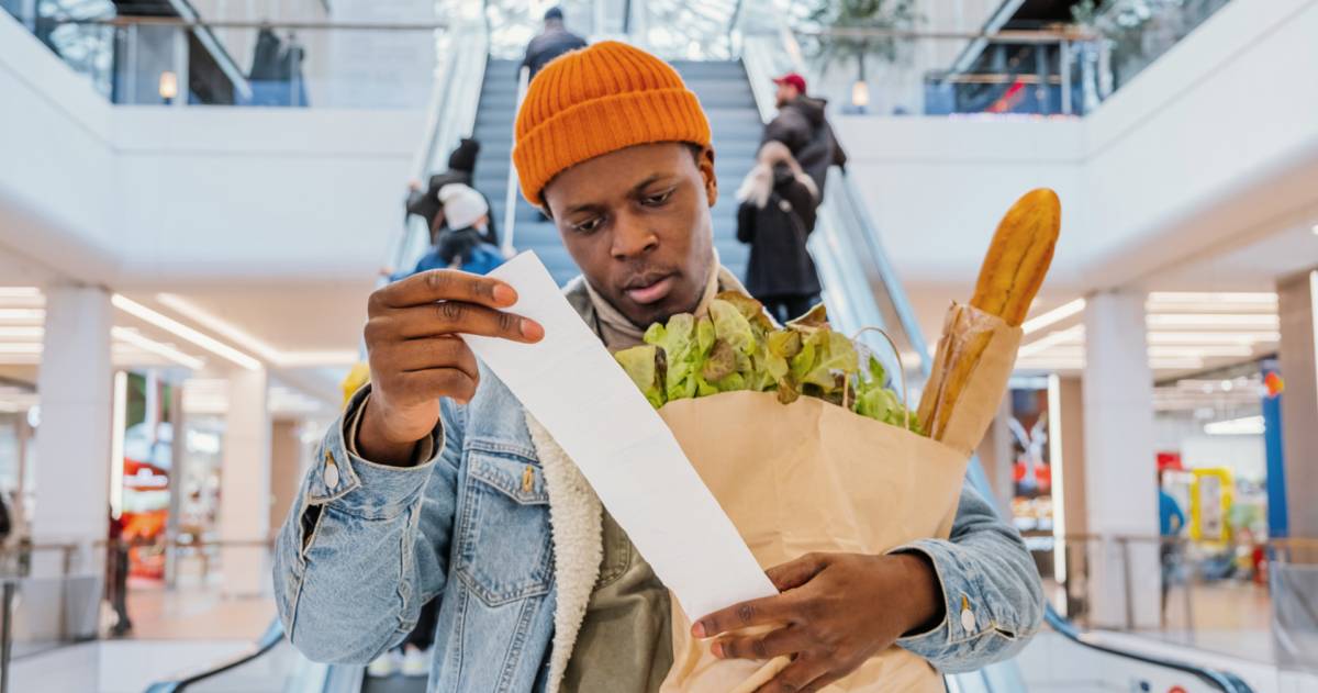 Een man heeft een zak met boodschappen vast en schrikt van de prijs