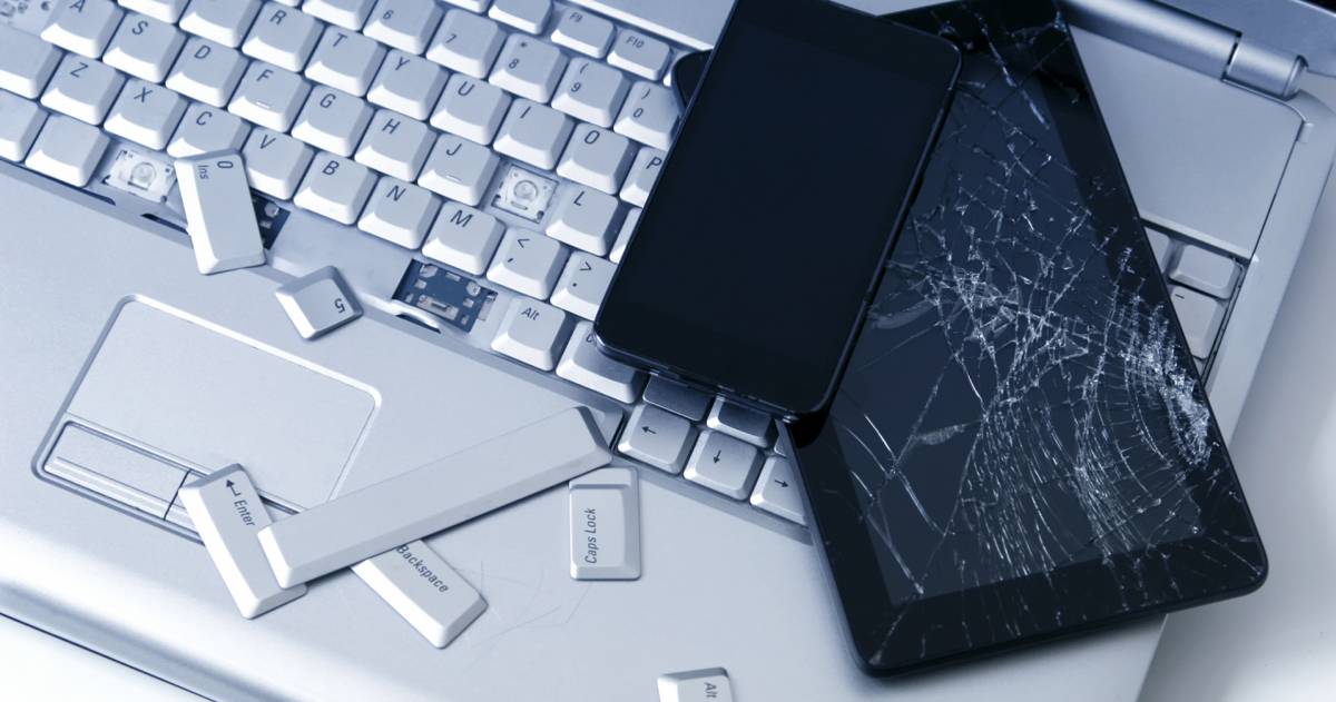 Een zilveren laptop met een kapot toetsenbord, een tablet met een kapot scherm en een telefoon